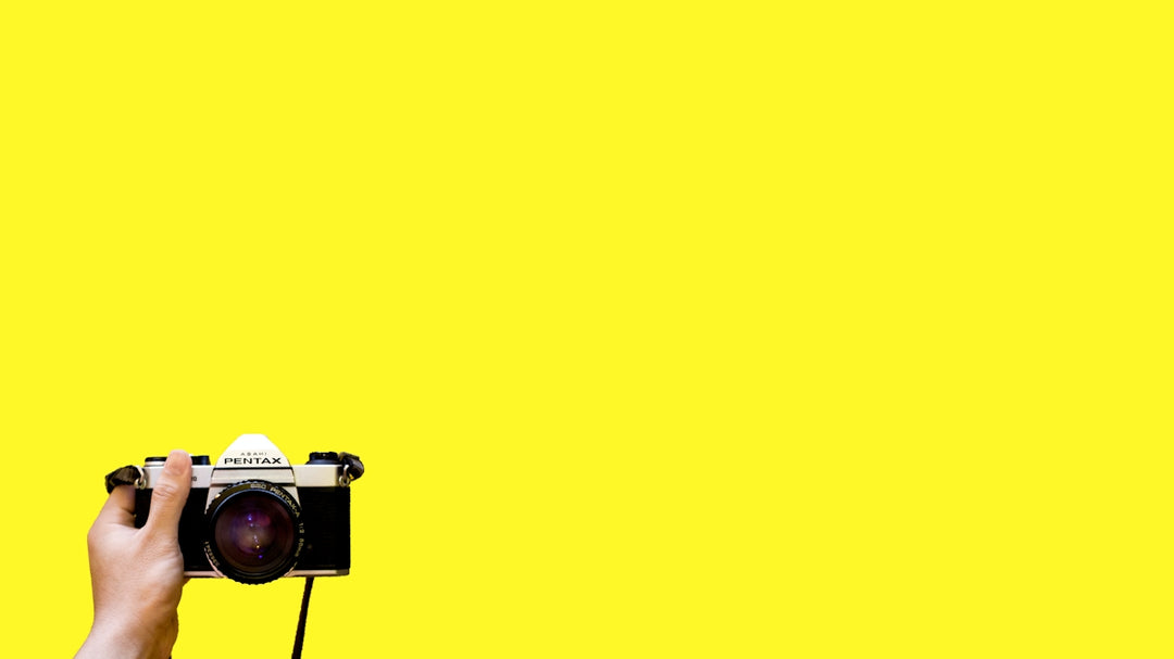 a person holding a camera in front of a yellow background