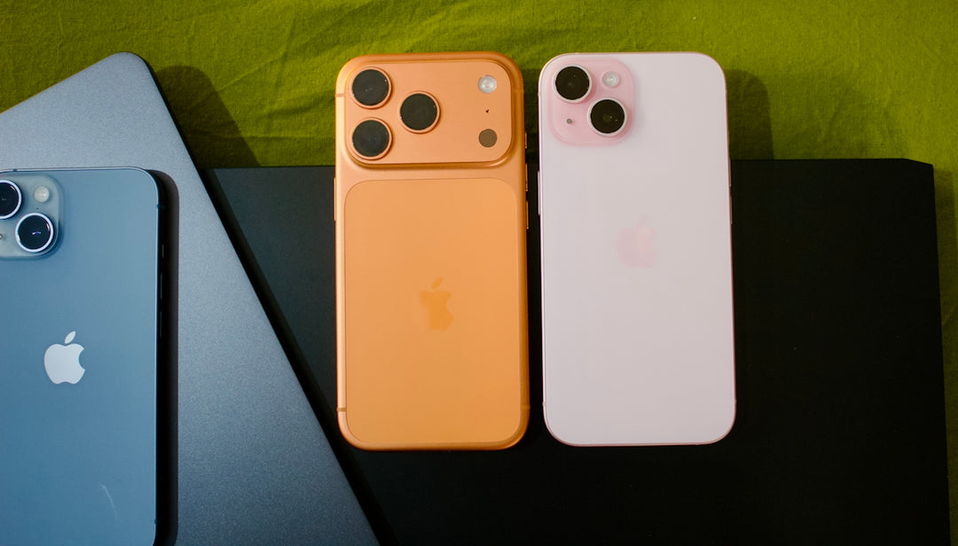 Three iphones in different colors on a dark surface