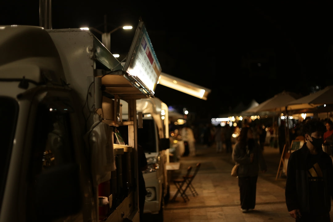 People walking at a night market with food trucks.
