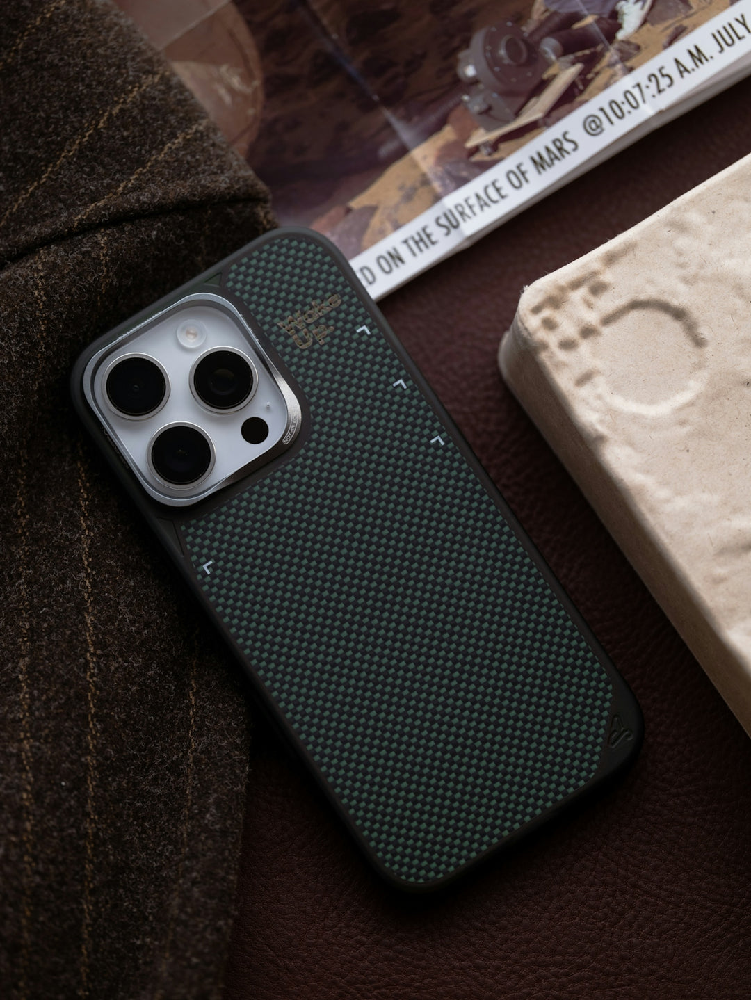 Dark textured smartphone case on brown fabric with white block.