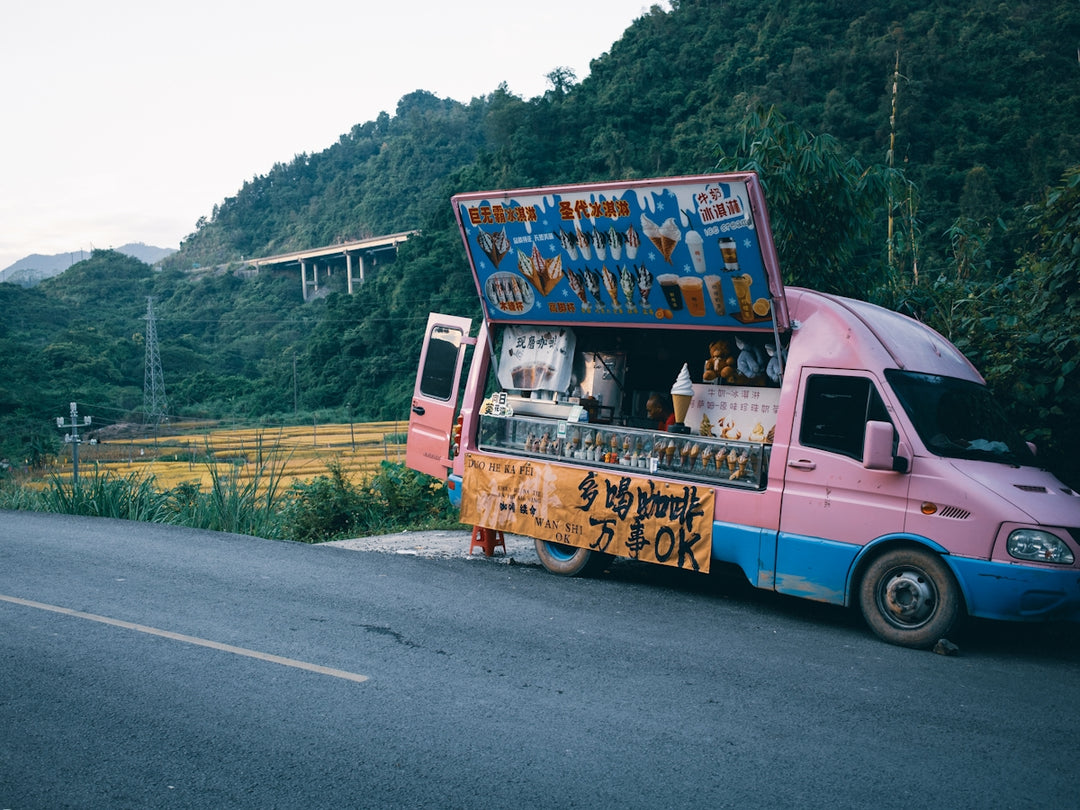 A colorful food truck parked roadside against a mountain backdrop.